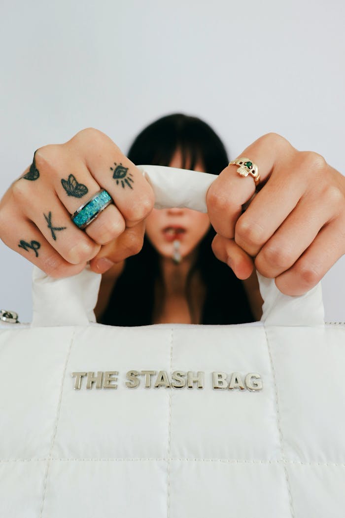 Home (DUPLICATE) Close-up of woman showcasing stylish bag and tattooed hands, conveying modern fashion vibe.