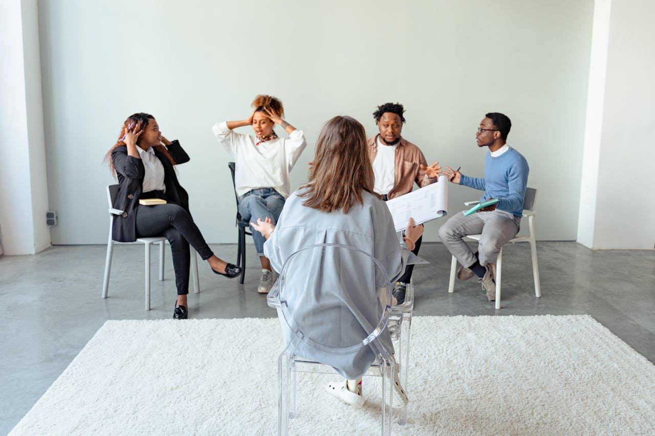 Services People engaging in a group therapy session indoors, discussing mental health topics.